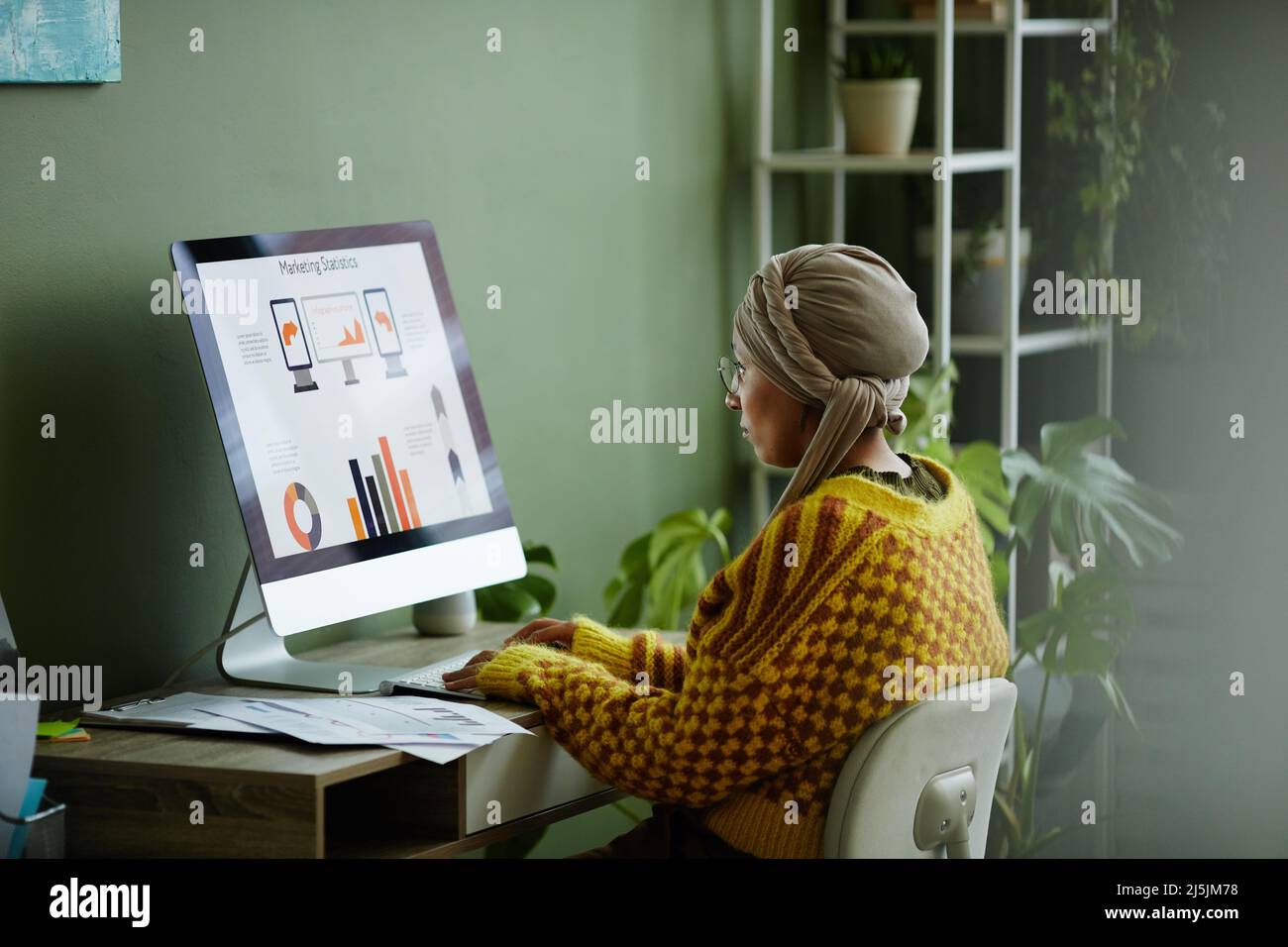 Portrait vibrant de la jeune femme d'affaires ethnique utilisant un ordinateur tout en travaillant à un bureau dans un bureau vert Banque D'Images