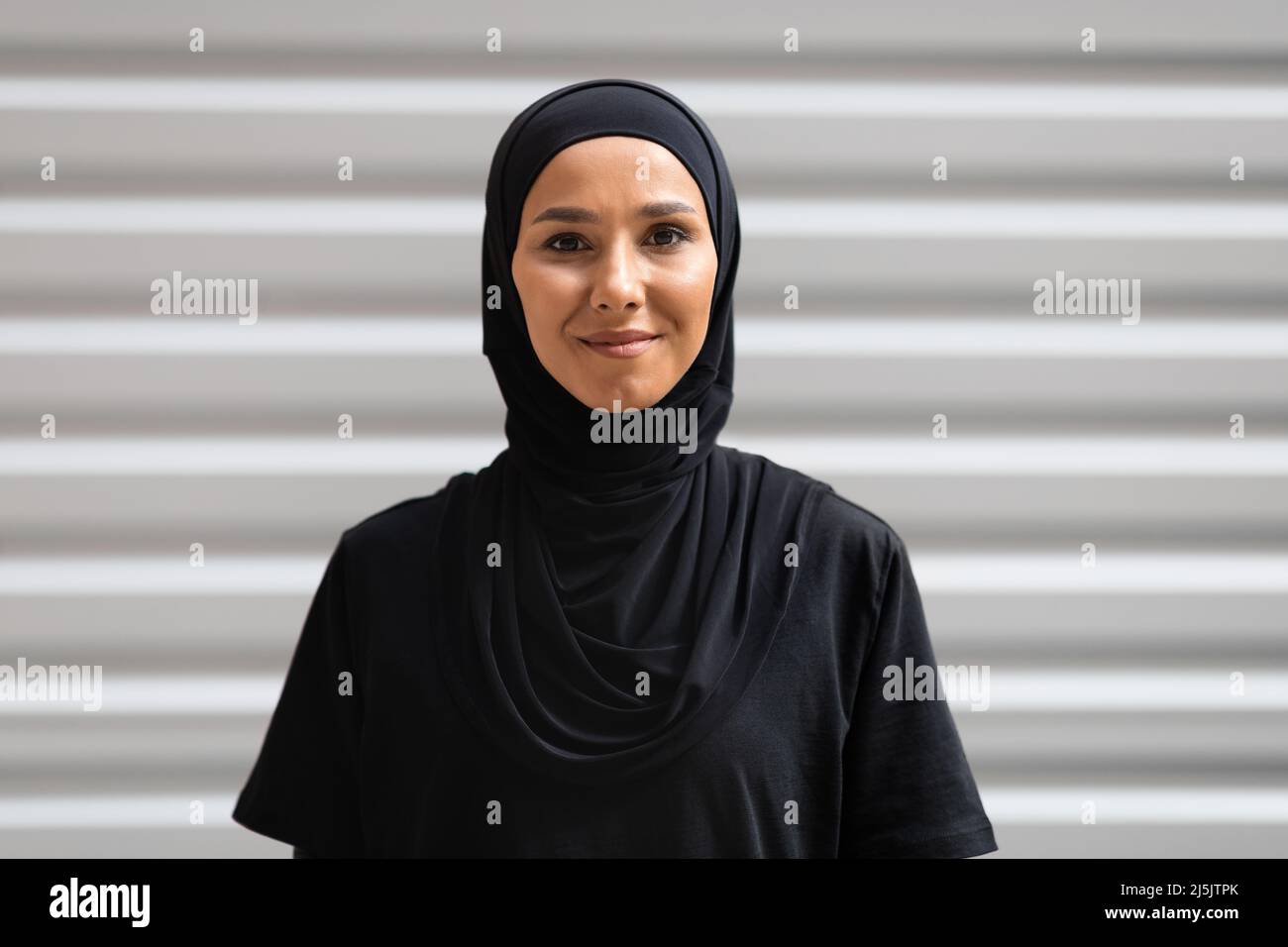 Souriante confiante jolie femme du Moyen-Orient millénaire en hijab regarder la caméra sur fond de mur, l'espace de copie Banque D'Images