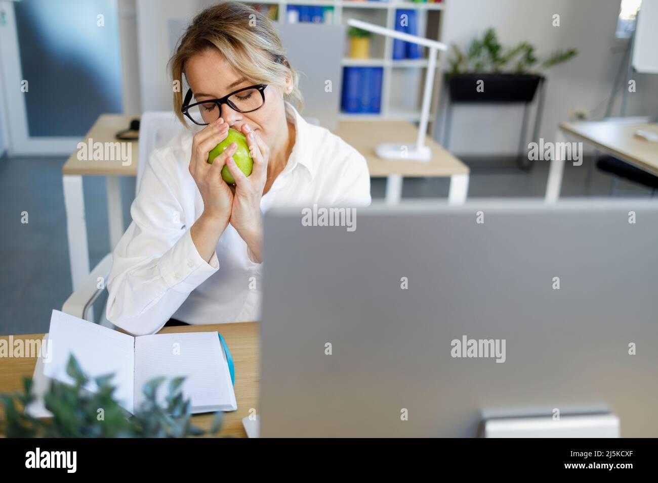 Un employé de bureau renifle une pomme verte parfumée tout en ayant une collation au travail Banque D'Images