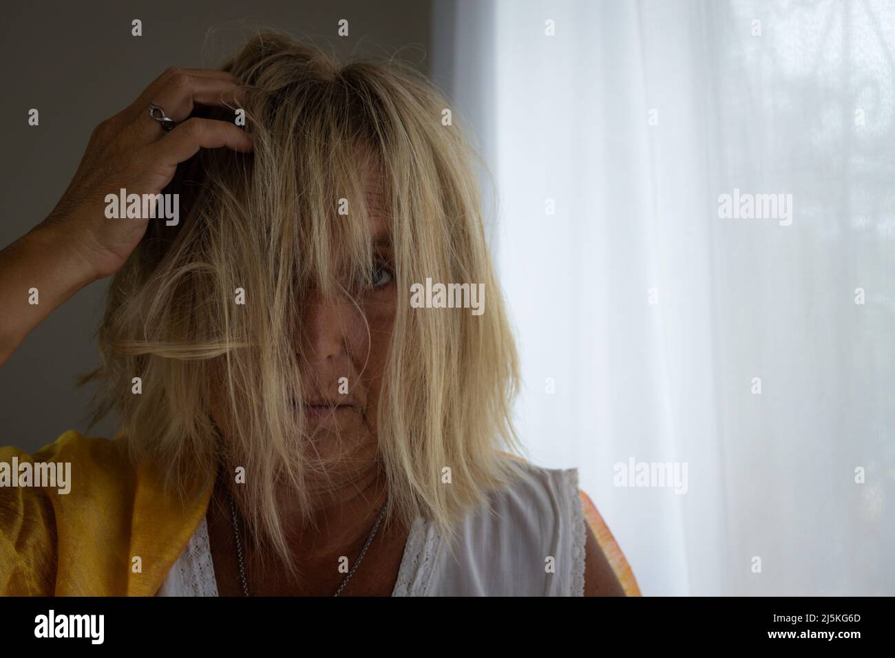 Femme blanche blonde de 50-60 ans avec cheveux touffés sur fond neutre. Concept de femme stressée. Banque D'Images