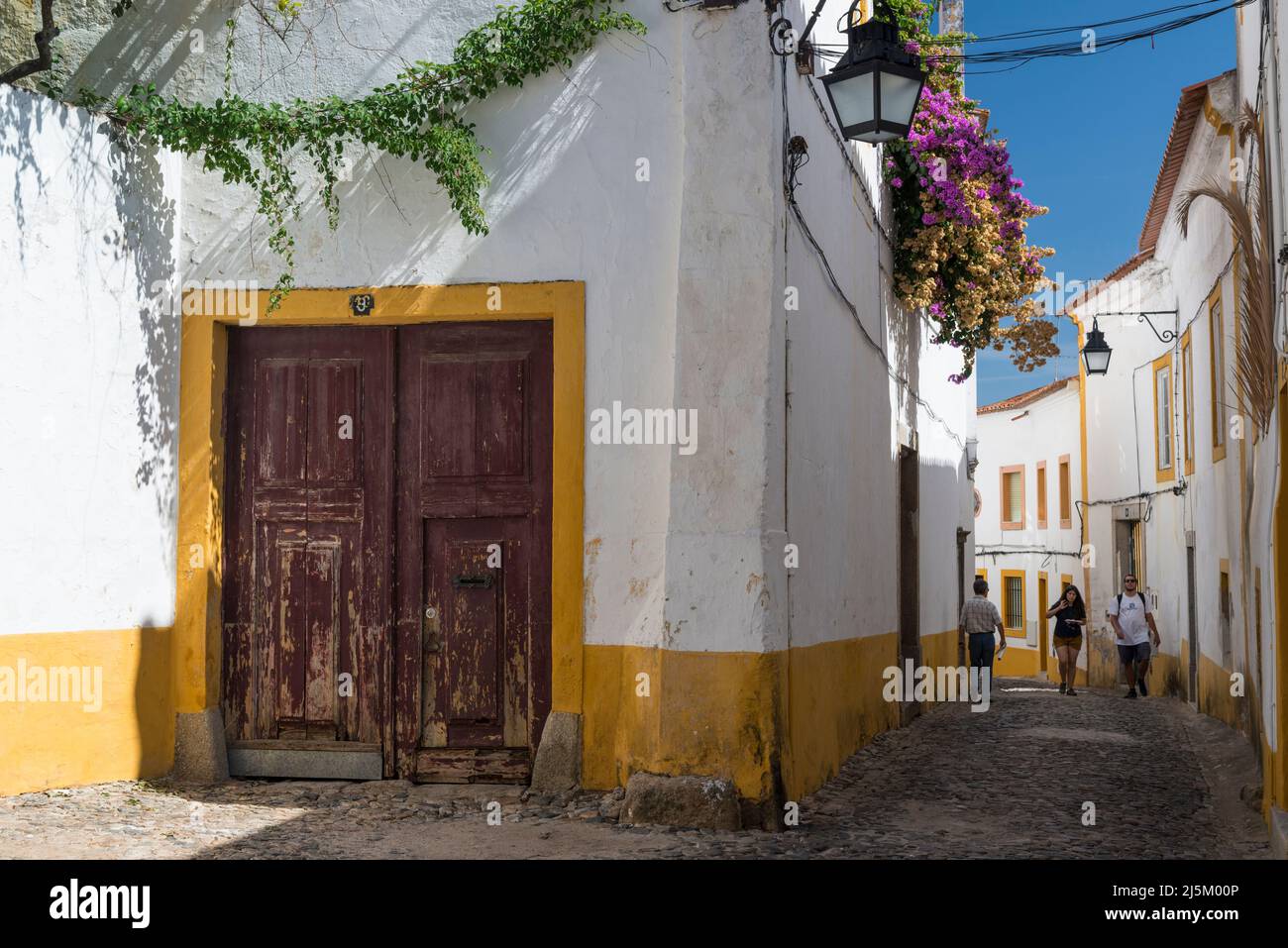 Trois personnes se promenant dans l'une des ruelles pittoresques bordées de galets avec des maisons blanches et jaunes dans le centre historique d'Evora, Portugal. Banque D'Images