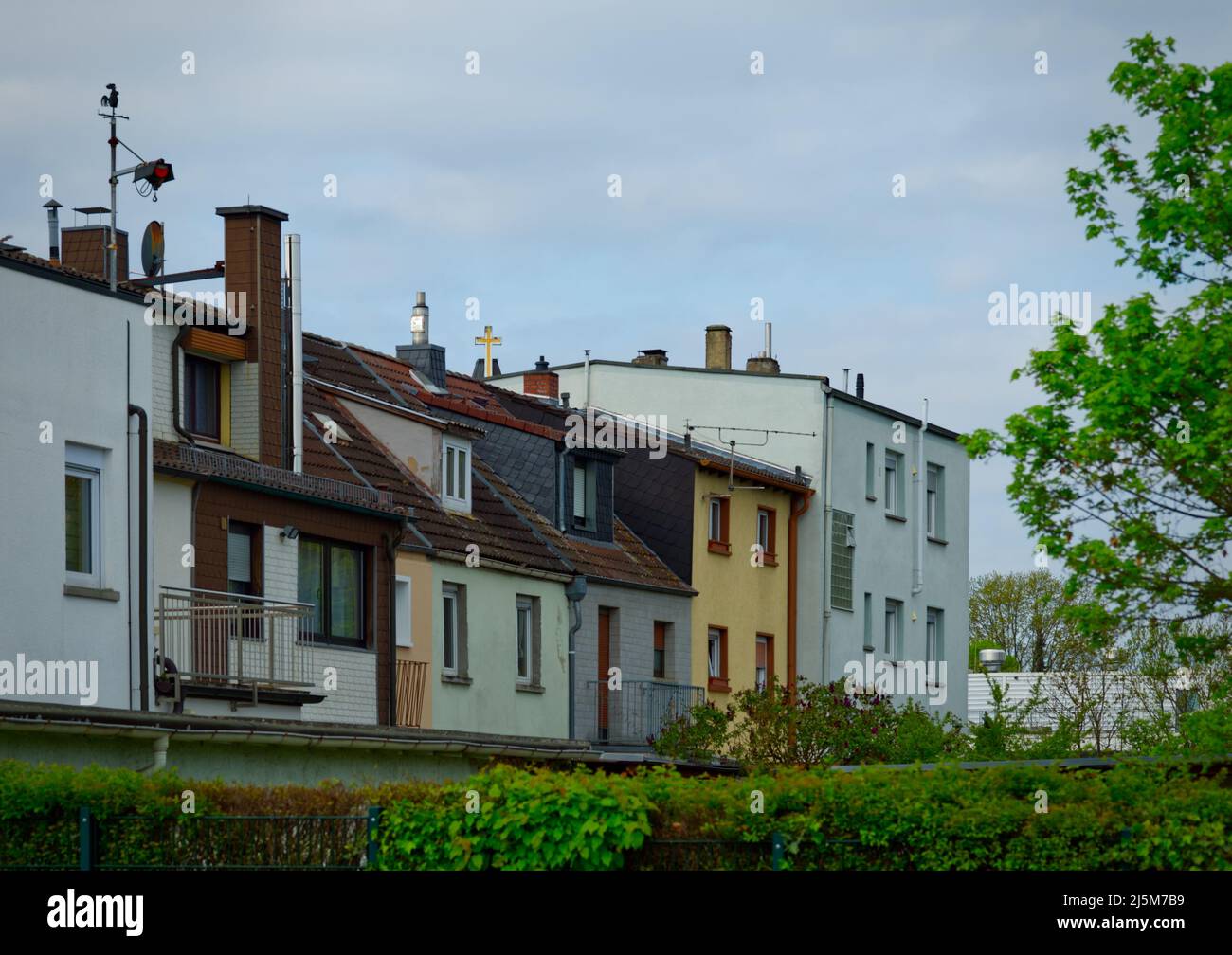 ligne de plusieurs bâtiments de banlieue dans différents tons avec cheminées et la croix jaune d'une église au centre Banque D'Images