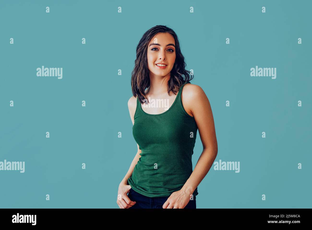 Jeune femme adulte portant un débardeur avec les mains sur les poches souriant regardant le portrait de studio d'appareil photo Banque D'Images
