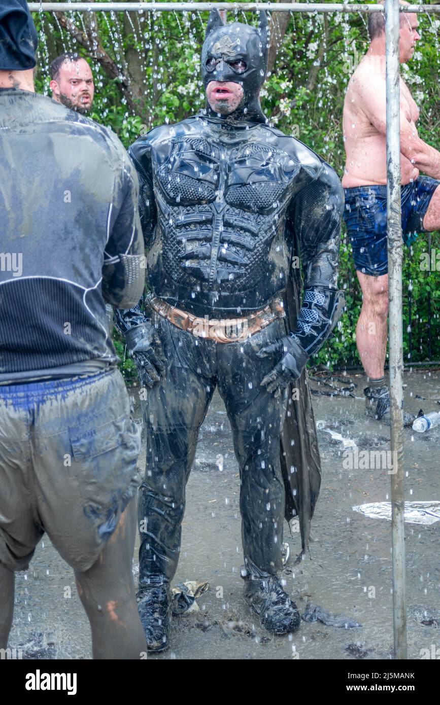 Homme en costume Batman qui s'entête dans la boue après la Maldon Mud Race, Essex, Royaume-Uni. Des activités caritatives s'amusent à traverser la boue de la rivière Blackwater à marée basse Banque D'Images