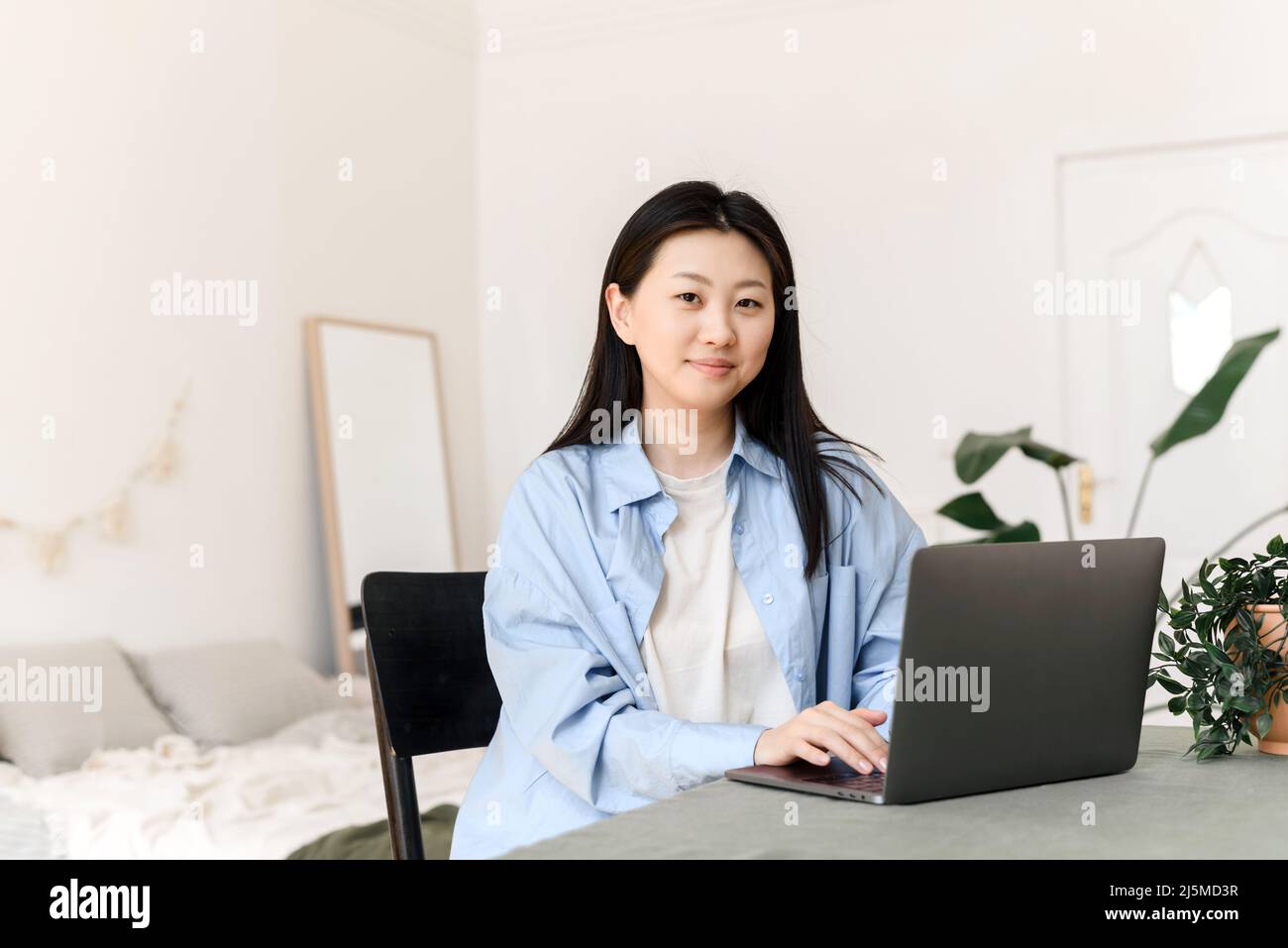 Jeune femme asiatique travaillant sur un ordinateur portable à la maison et regardant la caméra. Concept d'entreprise freelance Banque D'Images