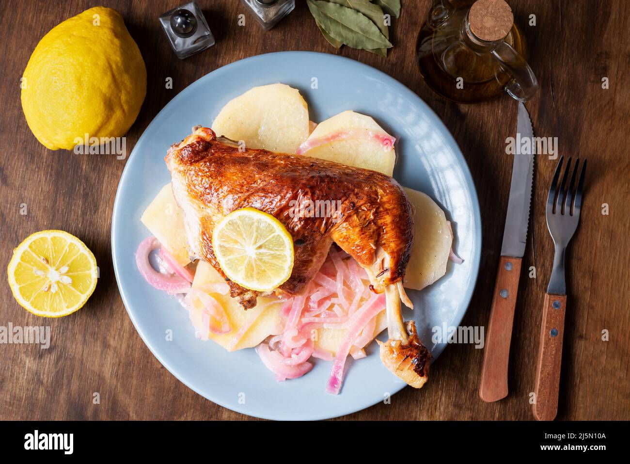Plat avec cuisse de poulet au citron, pommes de terre et oignon rouge, huile d'olive, citrons, sel et poivre en arrière-plan. Banque D'Images