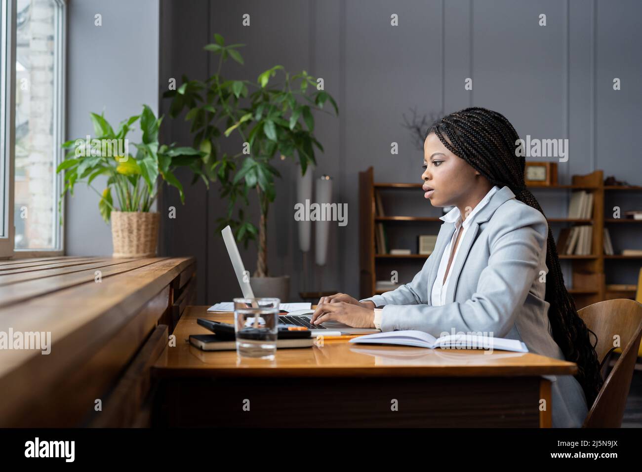 Une comptable à distance féminine noire ciblée prépare un rapport financier sur un ordinateur portable tout en travaillant à domicile Banque D'Images