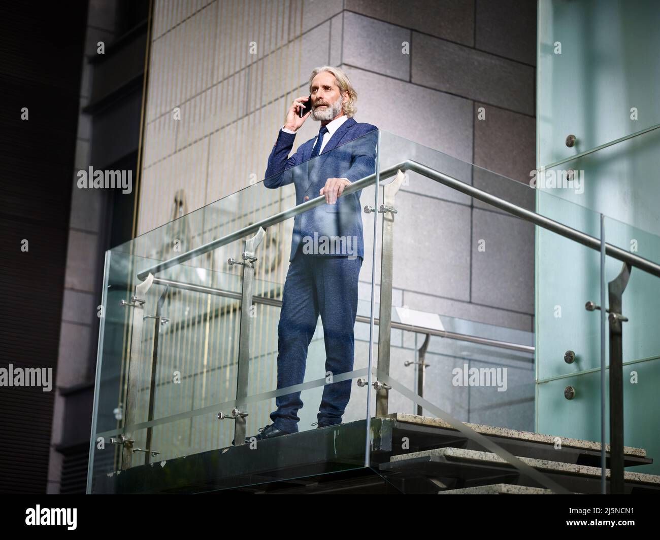 homme d'affaires caucasien mature se tenant au-dessus des escaliers faisant un appel à l'aide d'un téléphone cellulaire dans un bâtiment de bureau moderne Banque D'Images