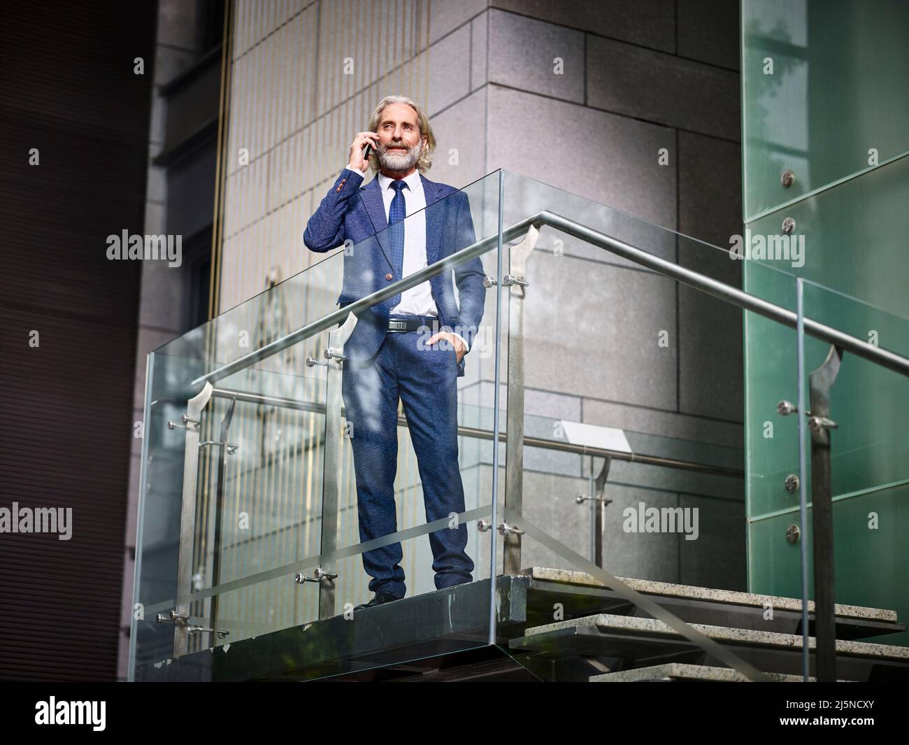 homme d'affaires caucasien mature se tenant au-dessus des escaliers faisant un appel à l'aide d'un téléphone cellulaire dans un bâtiment de bureau moderne Banque D'Images