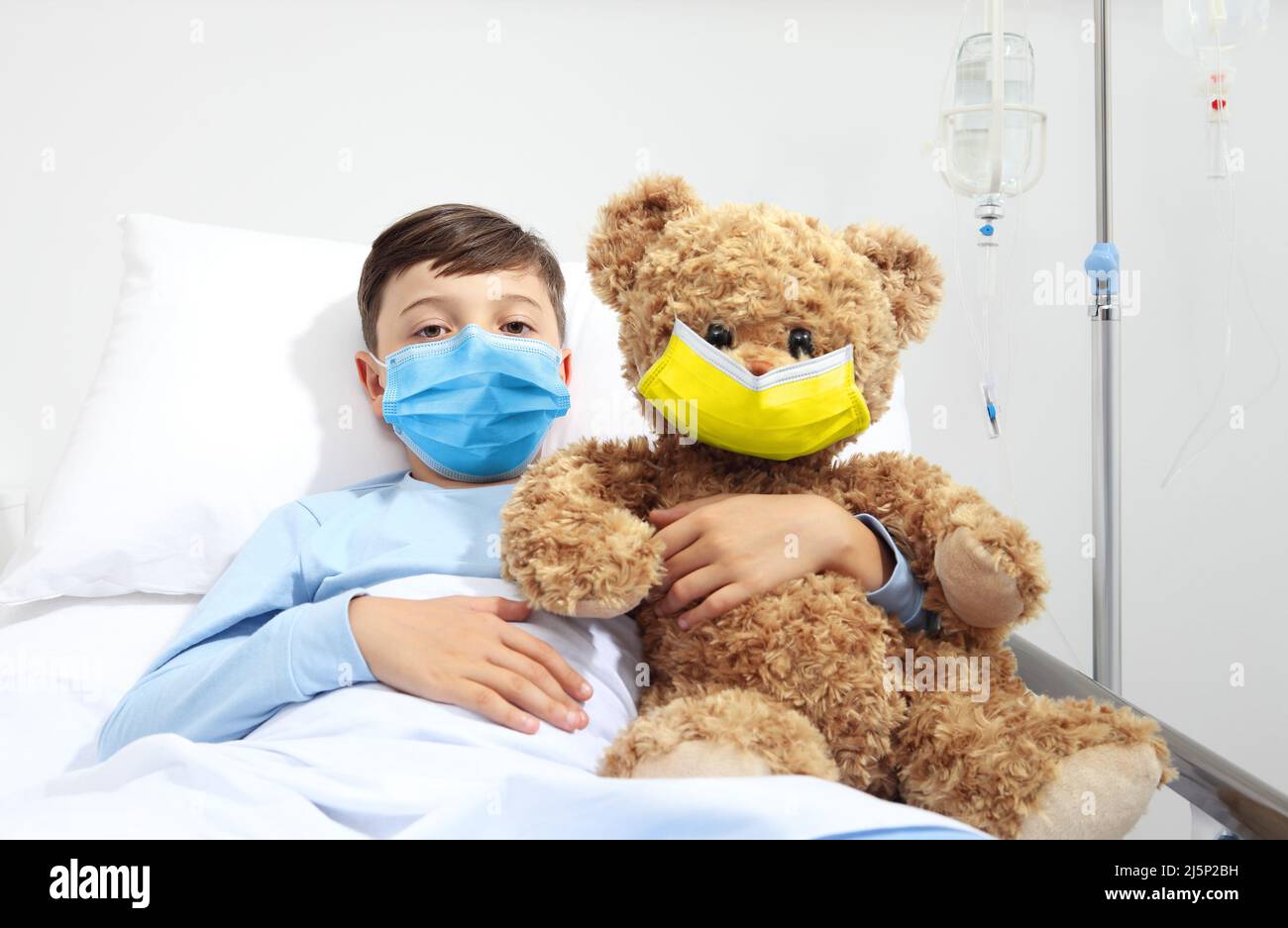 Aide humanitaire, aide à la protection médicale pour la guerre d'Ukraine, enfant dans le lit d'hôpital avec ours en peluche portant masque facial de protection jaune et bleu colo Banque D'Images