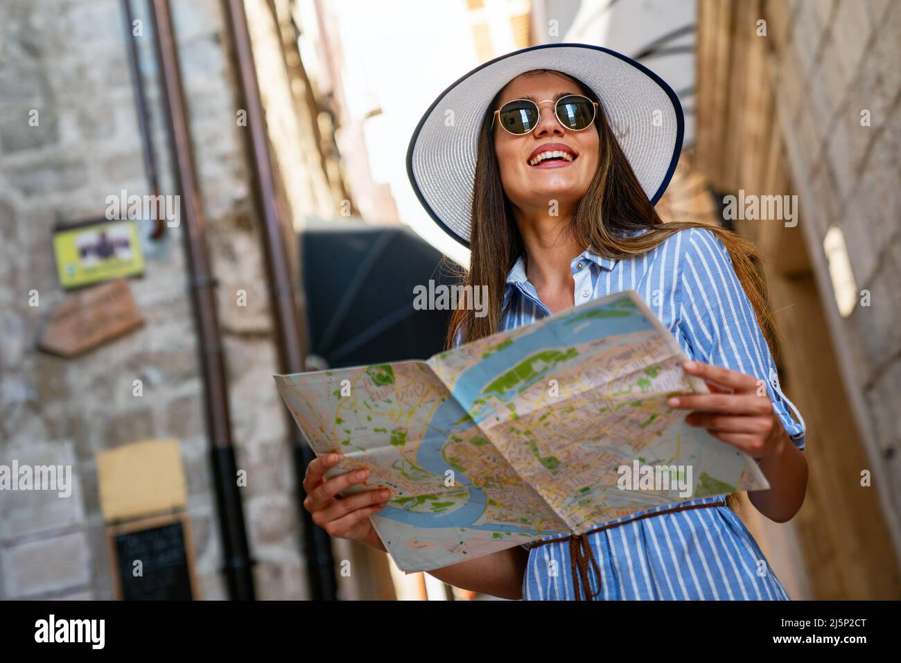 Une femme joyeuse avec un look tendance à la recherche de la direction sur la carte de position lors de voyages à l'étranger en été Banque D'Images