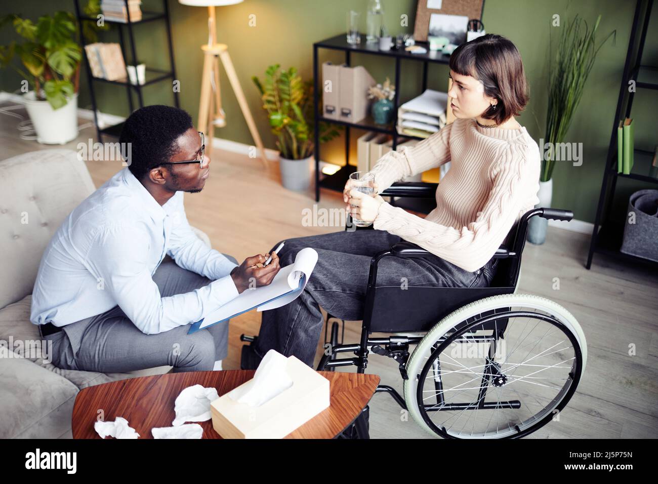 Jeune femme en fauteuil roulant ayant une séance de thérapie privée avec un psychologue pour apprendre à accepter un handicap Banque D'Images