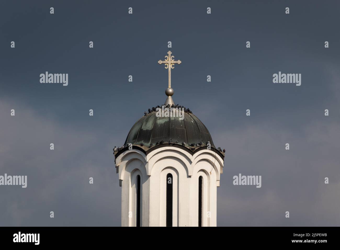 Pigeons se reposant et se prélassant au soleil sur le toit de cuivre de l'église, beffroi orthodoxe de l'église contre les nuages sombres de tempête Banque D'Images
