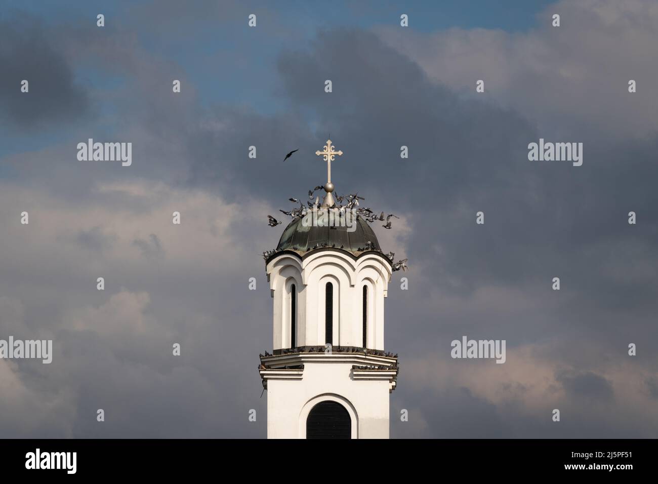 Un troupeau de pigeons survole le clocher de l'église contre des nuages sombres Banque D'Images