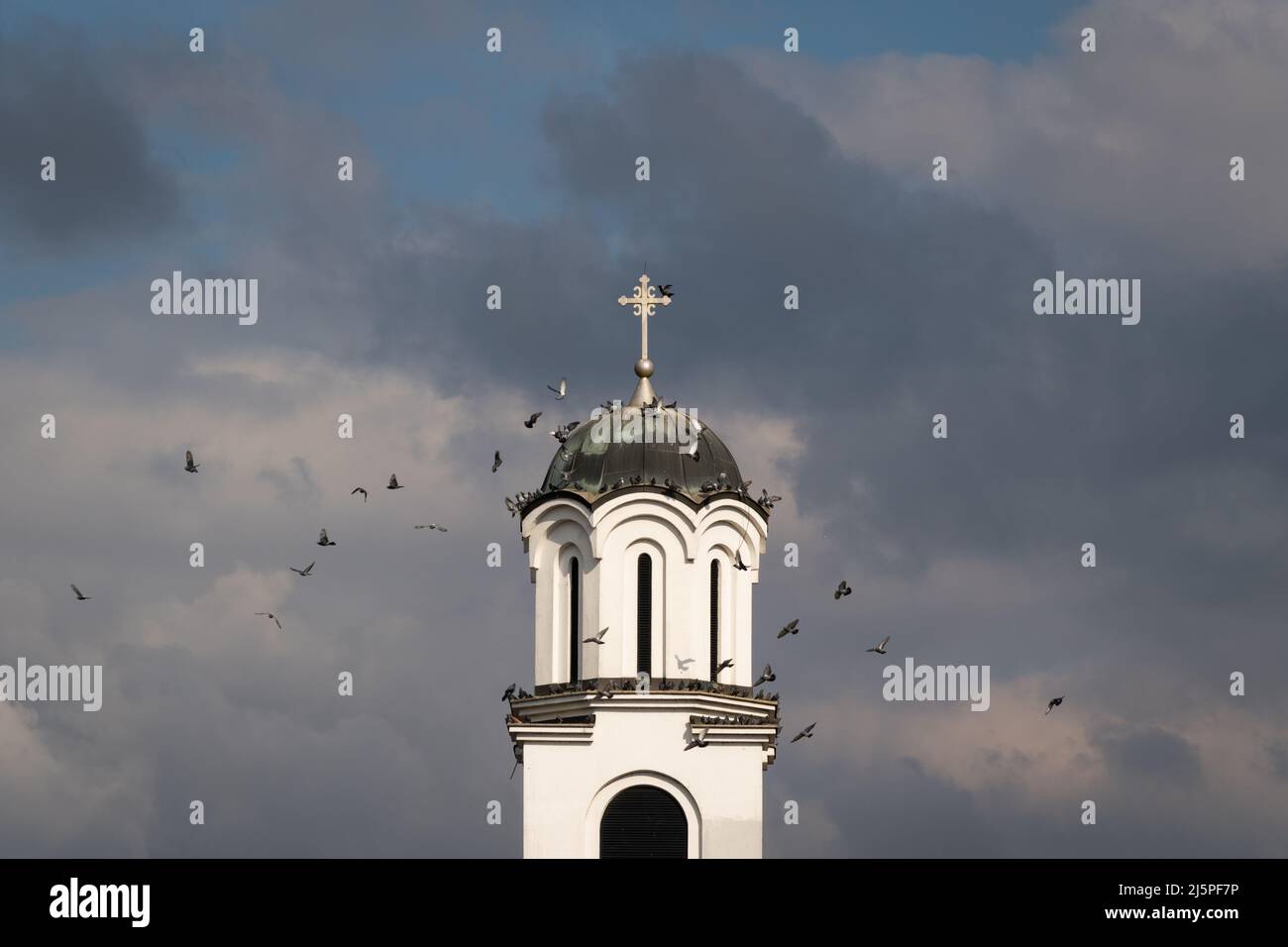 Un troupeau de pigeons survole le clocher de l'église contre des nuages sombres Banque D'Images