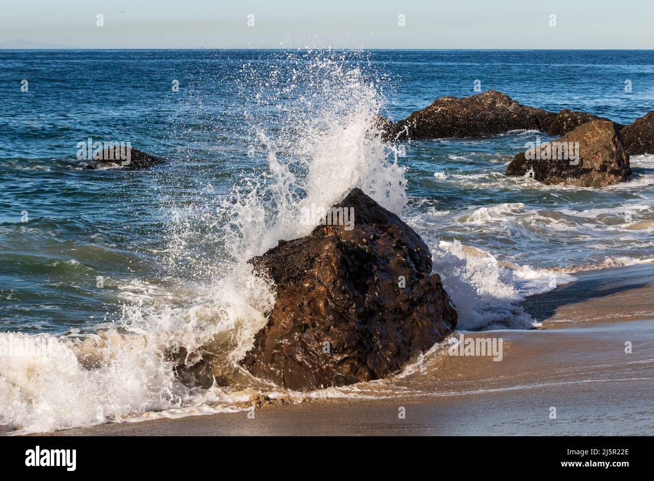 La vague s'est déferlante contre le rocher à Malibu, en Californie. L'eau s'étire de la plage. Océan Pacifique, ciel bleu à distance. Banque D'Images