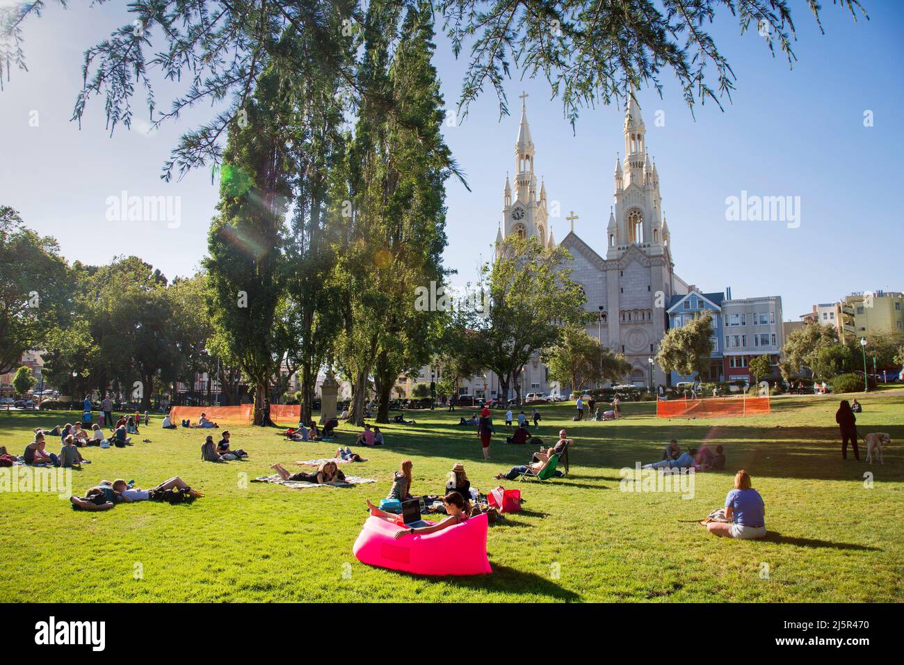 Etats-Unis, Washington Square Park à San Francisco des personnes se posant sur la pelouse avec l'église Saints Pierre et Paul en arrière-plan et une femme sur une wor fatboy Banque D'Images