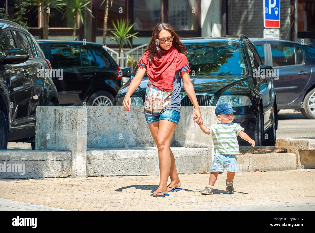 Mère et petit fils marchent dans la rue d'omis contre les voitures garées sur le lot le jour ensoleillé. Femme et tout-petit garçon profitent de vacances d'été en Croatie Banque D'Images