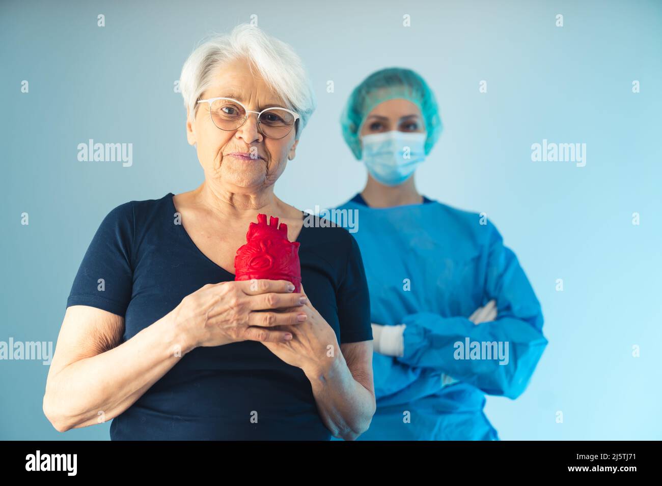 Femme médecin debout derrière la femme européenne âgée reconnaissante tenant un cœur artificiel rouge moyenne shot studio tourné bleu fond de santé concept . Photo de haute qualité Banque D'Images