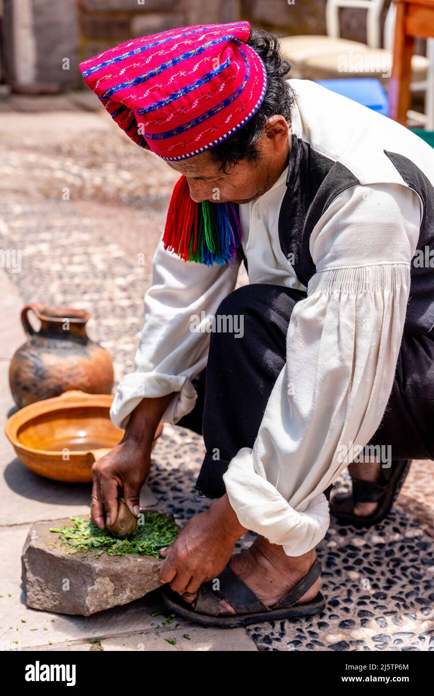 Un homme Taquileno dans les herbes traditionnelles de broyage de Costume, île de Taquile, lac Titicaca, Puno, Pérou. Banque D'Images