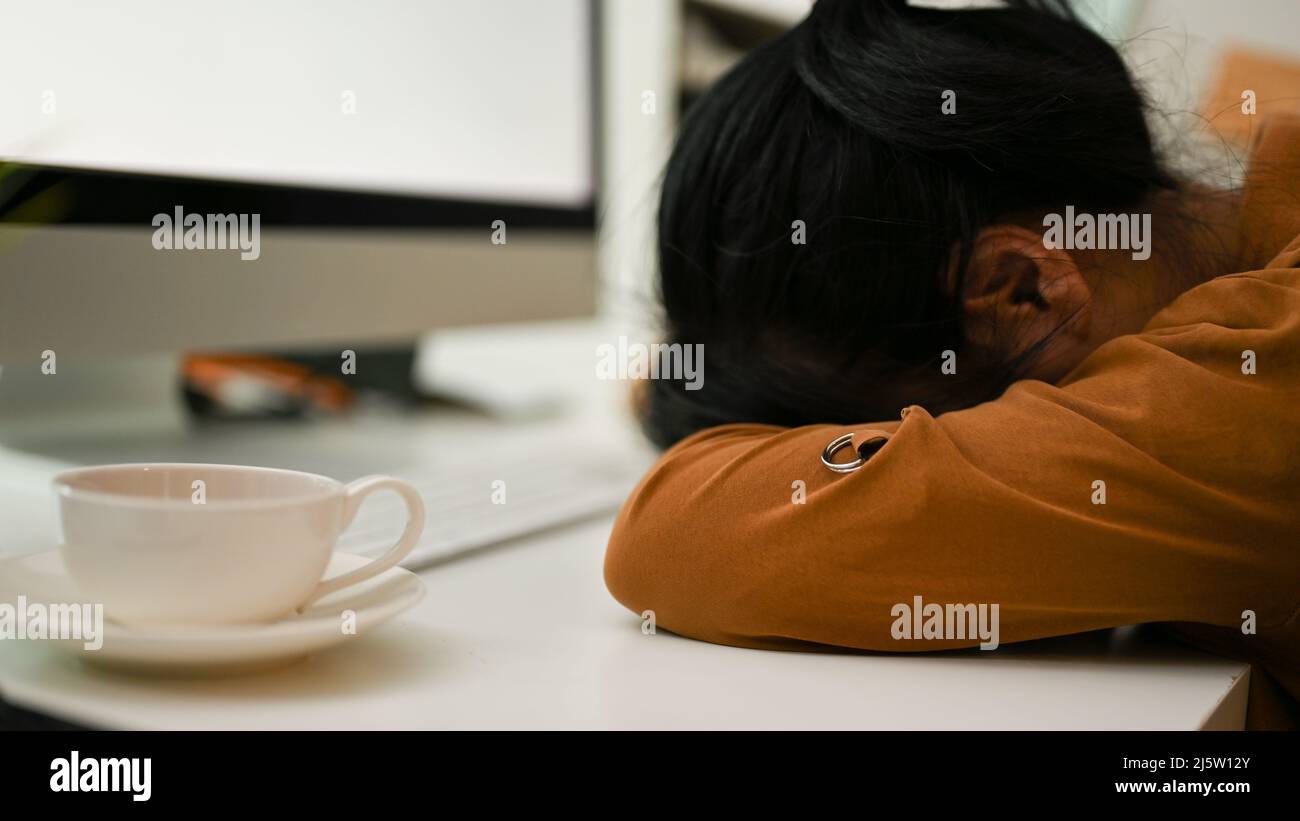 Une employée de bureau fatiguée a posé la tête sur la table, dormez sur la table du bureau. Manque d'énergie, épuisé, frustré. Banque D'Images