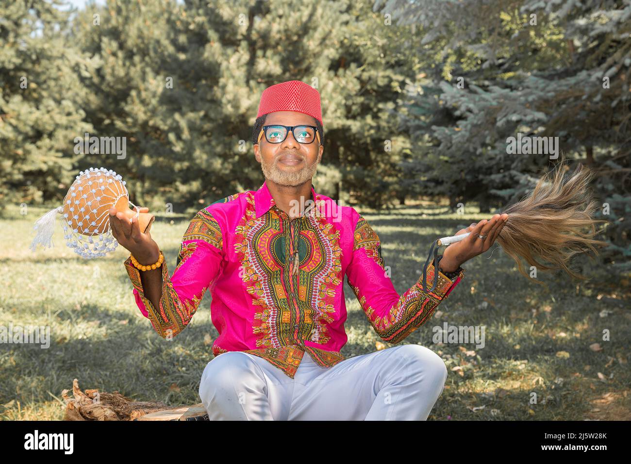 Le beau homme africain dans un costume national joue un tambour ethnique, djembe. Banque D'Images