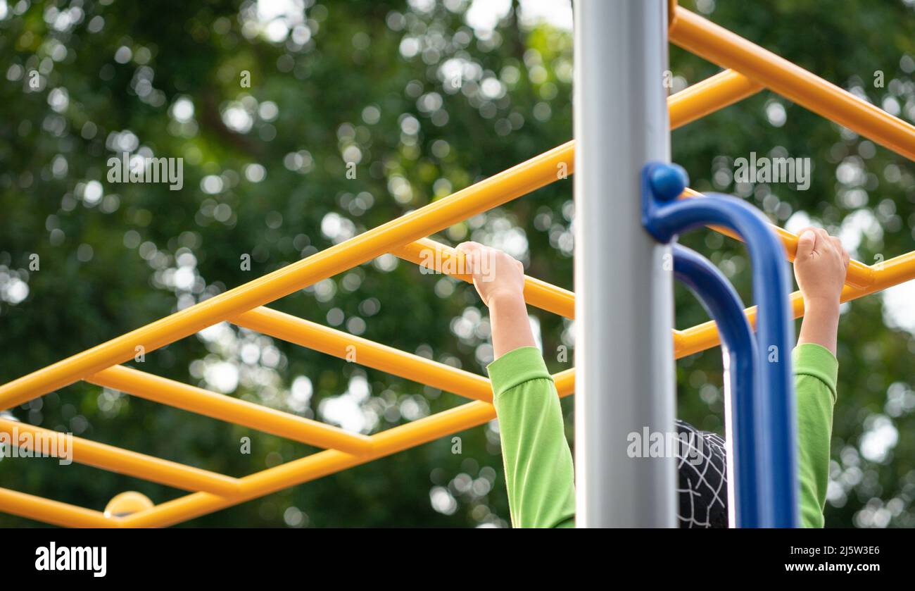 Enfants non reconnus jouant sur un équipement de terrain de jeu pour enfants, en plein air. Vue rapprochée des mains des enfants sur les barres de singes. Banque D'Images