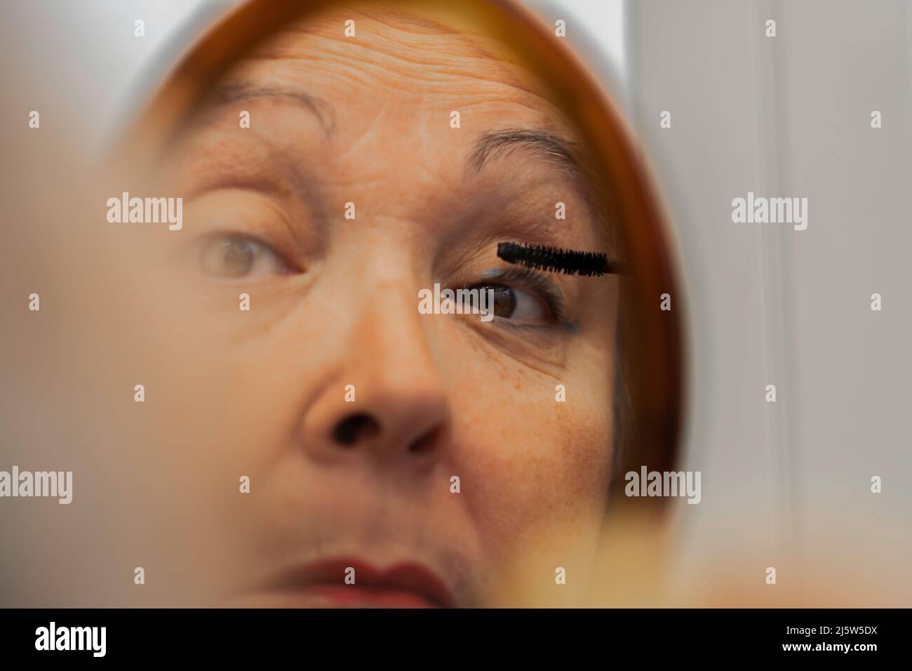 femme plus âgée peignant ses cils devant un miroir Banque D'Images
