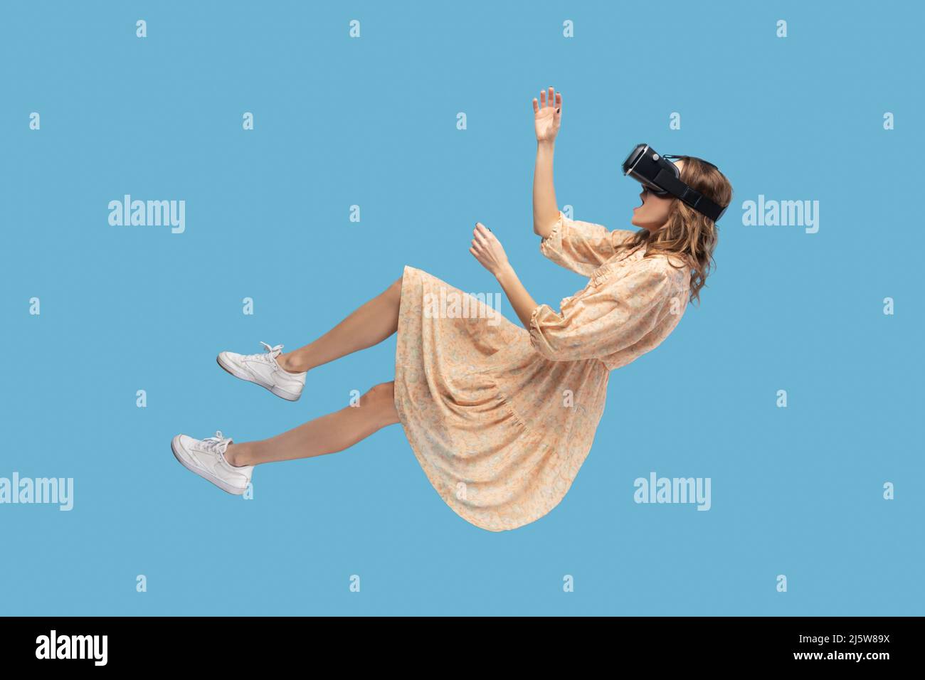 stupéfait surprise gamer fille planant dans l'air, en lévitant avec des lunettes de réalité virtuelle sur la tête, jouant au jeu par le casque vr, flottant dans le cyberespace. studio en intérieur tourné isolé sur fond bleu Banque D'Images