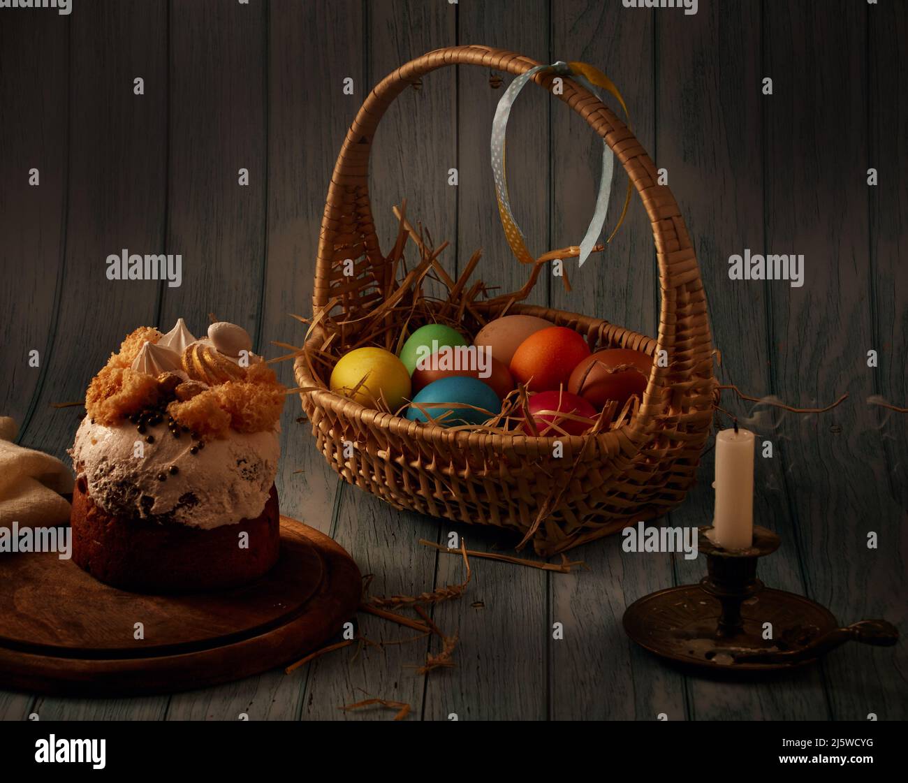 Gâteau de Pâques, un panier avec des œufs de couleur, un chandelier de bronze avec une bougie éteinte, avec un fond flou Banque D'Images
