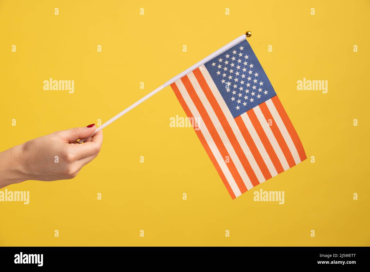 Profil vue latérale gros plan de la main humaine tenant le drapeau national des États-Unis. États-Unis d'Amérique. Journée nationale d'indépendance - 4th juillet. Studio d'intérieur isolé sur fond jaune. Banque D'Images