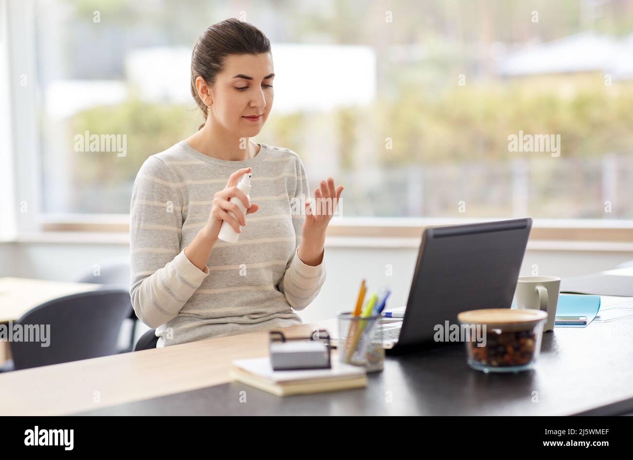 femme vaporisant de l'assainisseur pour les mains au bureau à domicile Banque D'Images