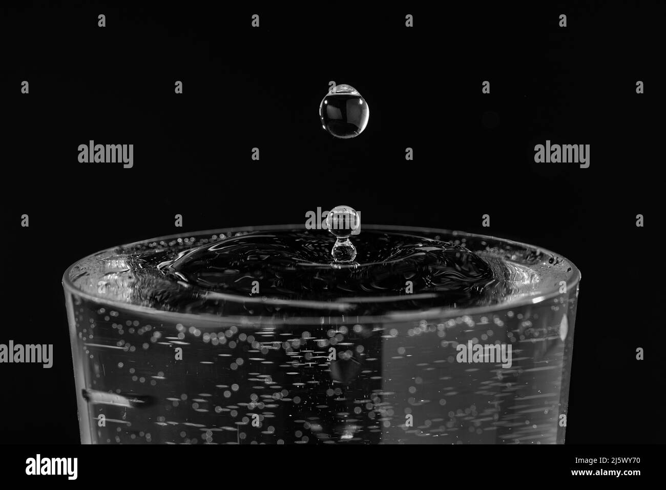 Gros plan d'une seule goutte d'eau qui frappe la surface, en noir et blanc Banque D'Images