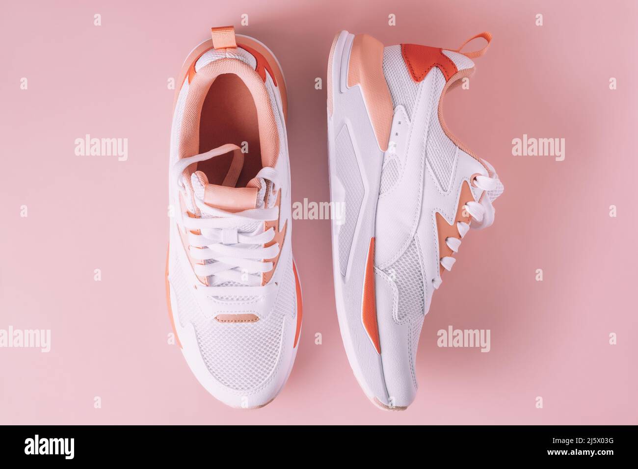 Sneakers blanches pour femme avec inserts corail sur fond rose. Vue de dessus. Pose à plat. Banque D'Images