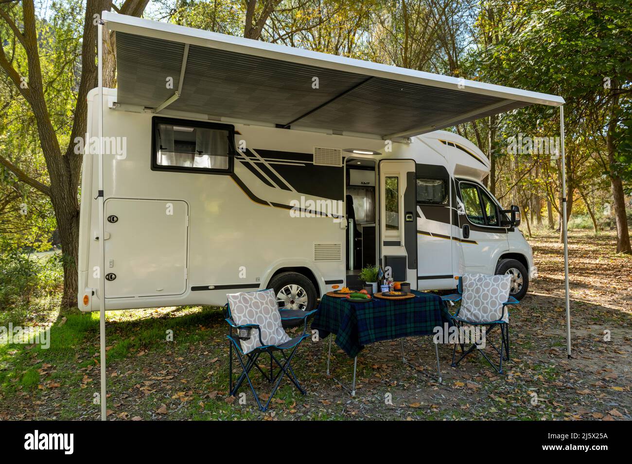 Motor home au camping avec une table et des chaises à l'extérieur du véhicule et prêt à manger et à boire. Banque D'Images