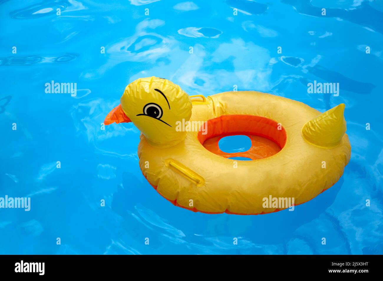Jouet gonflable de caneton en plastique jaune dans une piscine bleue avec de l'eau Banque D'Images