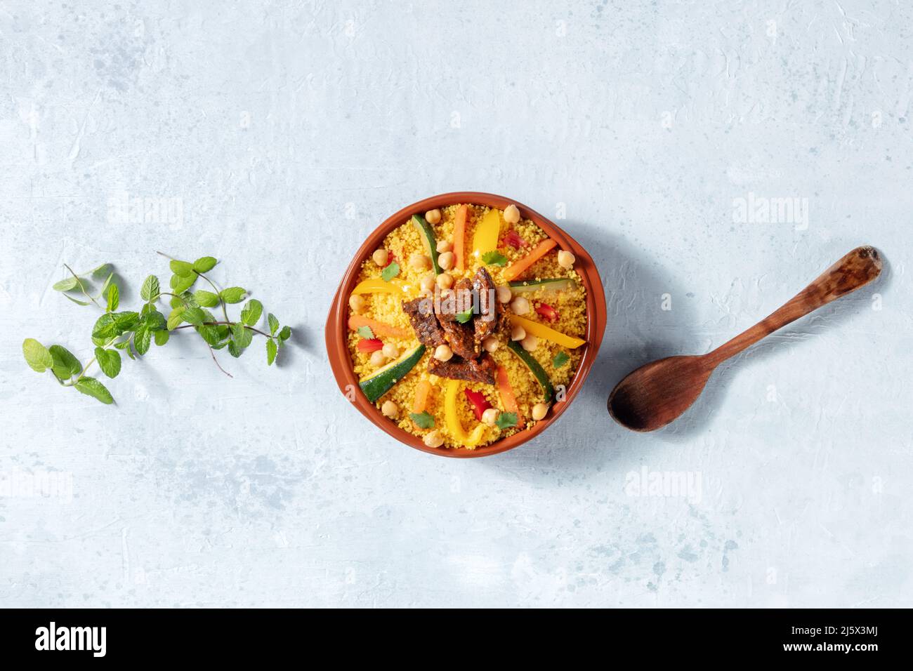 Couscous à la viande et aux légumes, dîner marocain festif, plan d'eau au plafond avec espace de copie, herbes fraîches et une cuillère en bois Banque D'Images