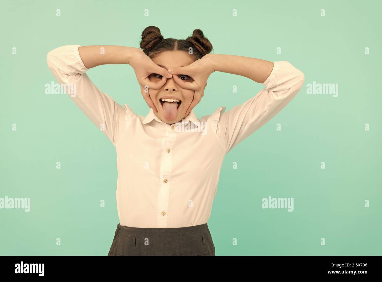 Heureux enfant d'âge scolaire faire des doigts masque super-héros collant la langue hors fond bleu, jouant Banque D'Images