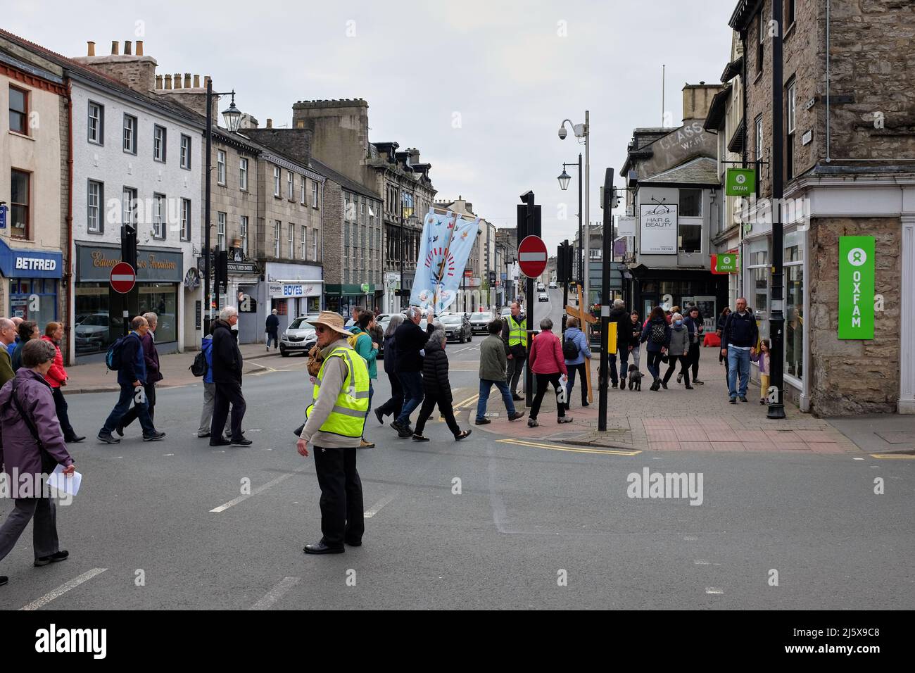 Procession de Pâques avec une bannière traversant la rue aux feux de circulation à Kendal, Cumbria, Royaume-Uni avec l'homme en hiviz veste regardant Banque D'Images