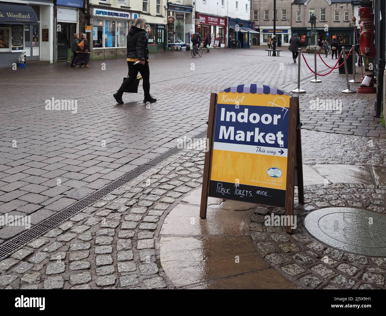 Signe faisant la promotion du marché intérieur avec une personne qui le passe, probablement en ignorant les plus petites boutiques pour les plus grands magasins à Kendal, Cumbria, Royaume-Uni Banque D'Images