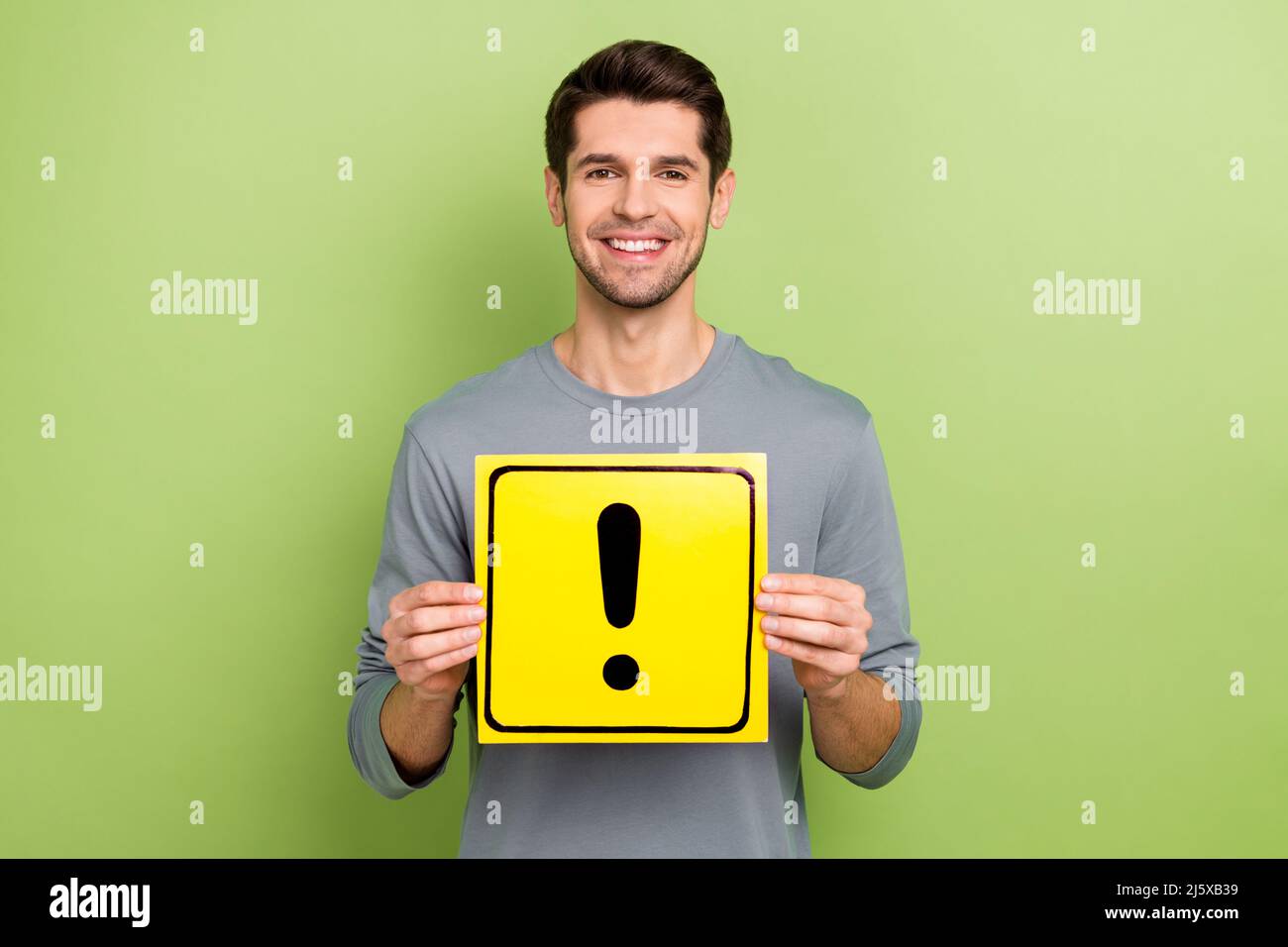 Photo de beau jeune brunet gars tenir signe usure tendance tissu isolé sur fond vert Banque D'Images
