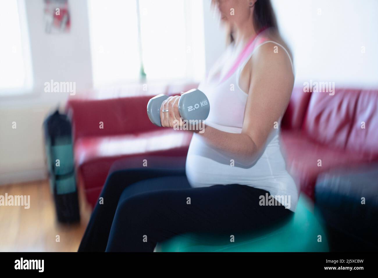 Femme enceinte s'exerçant avec des haltères sur le ballon de fitness à la maison Banque D'Images