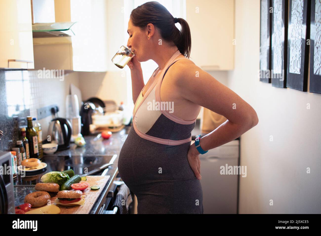 Femme enceinte buvant et mangeant dans la cuisine Banque D'Images