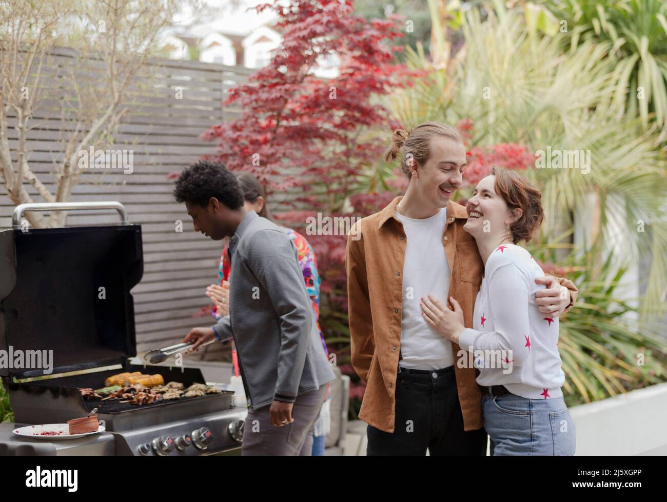 Joyeux jeune couple en train de profiter du barbecue sur le patio avec des amis Banque D'Images