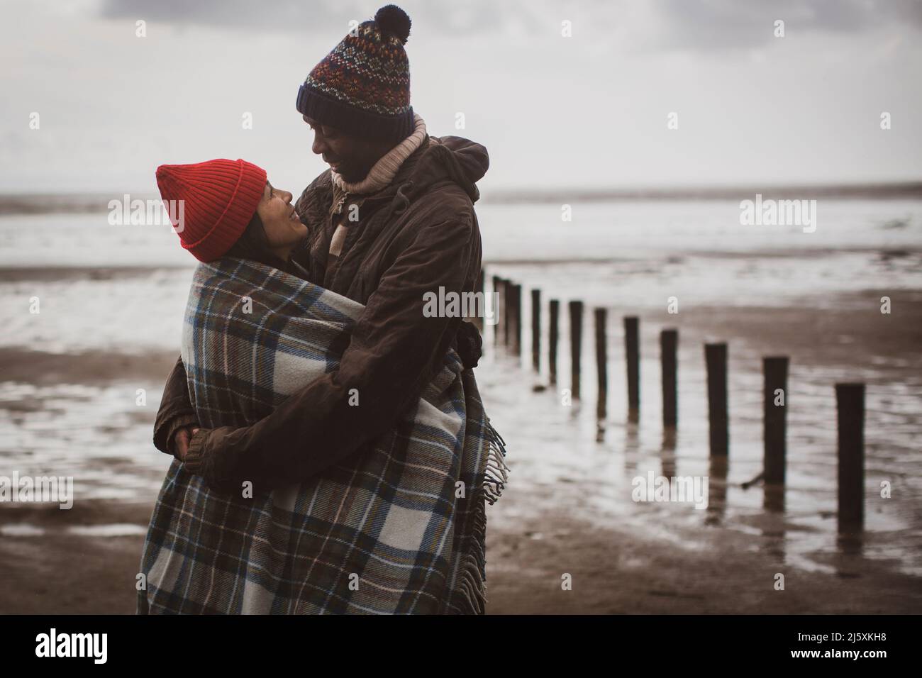 Couple heureux enveloppé dans une couverture sur la plage d'hiver Banque D'Images