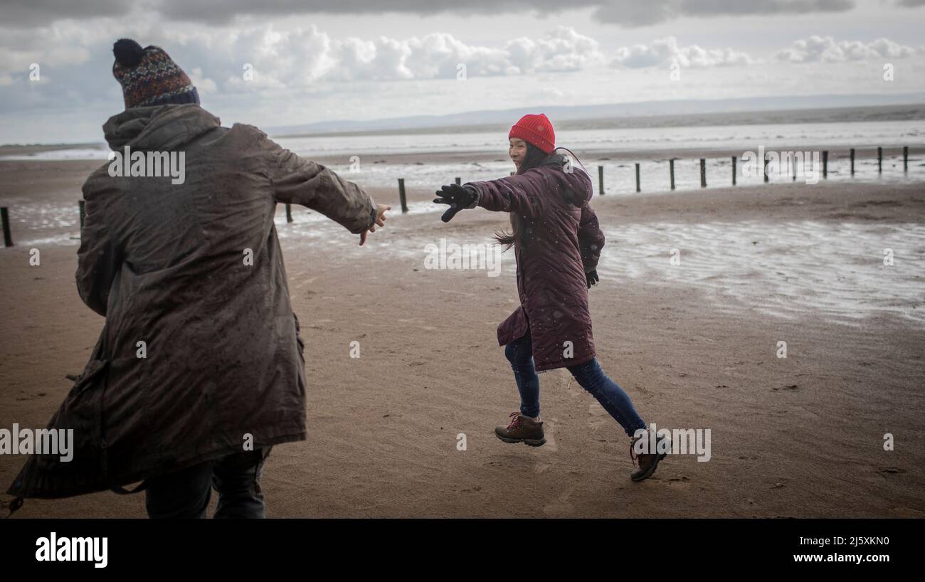 Couple joueur en vêtements chauds courant sur la plage d'hiver de l'océan Banque D'Images