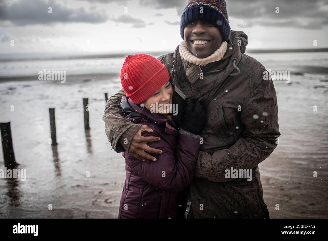 Couple heureux en vêtements chauds qui embrasse la plage d'hiver Banque D'Images