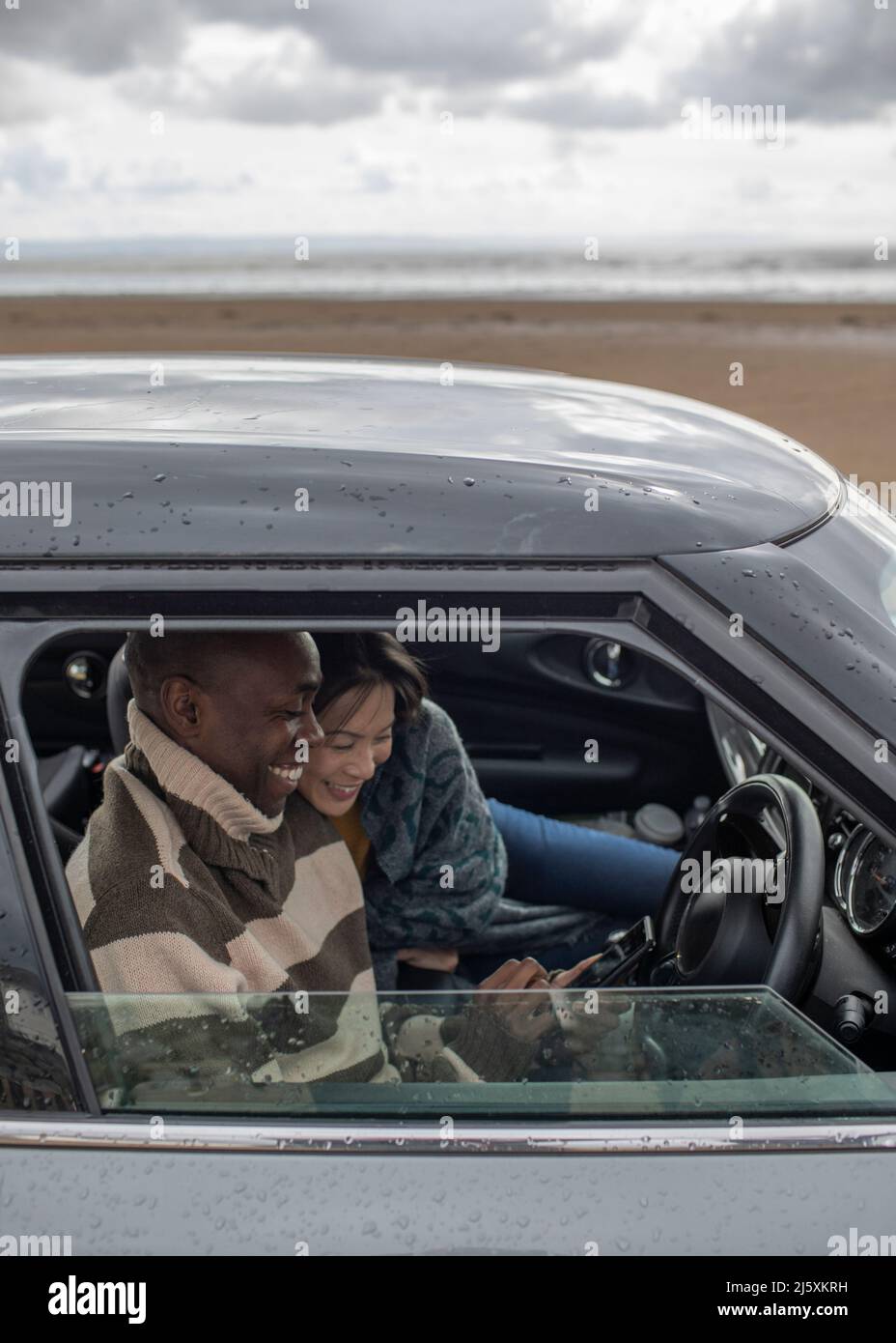 Couple heureux utilisant un smartphone à l'intérieur de la voiture sur la plage d'hiver Banque D'Images