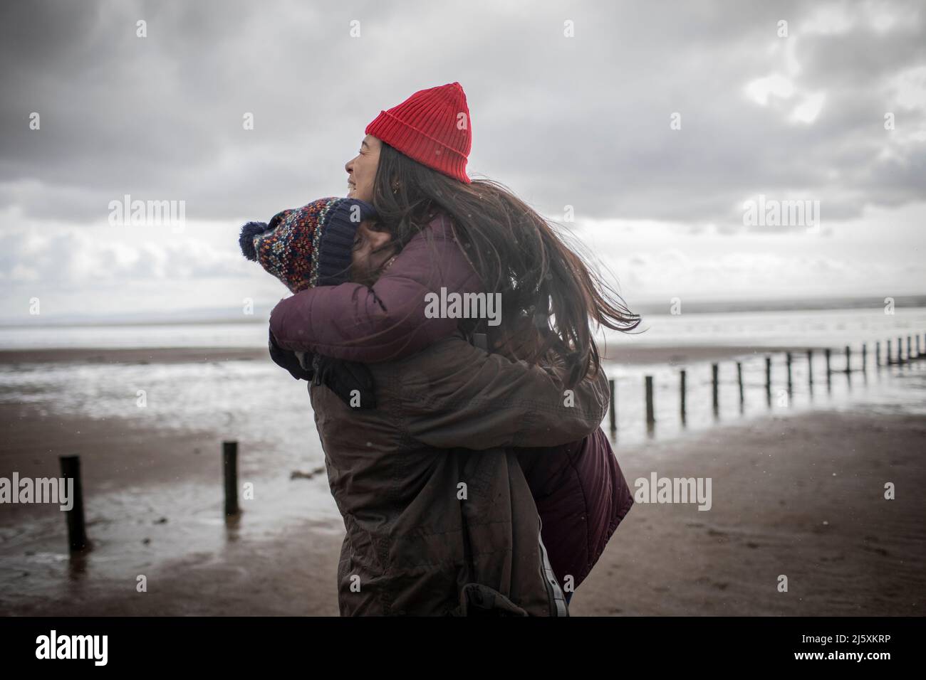 Couple affectueux et heureux qui s'enserre sur la plage humide d'hiver Banque D'Images