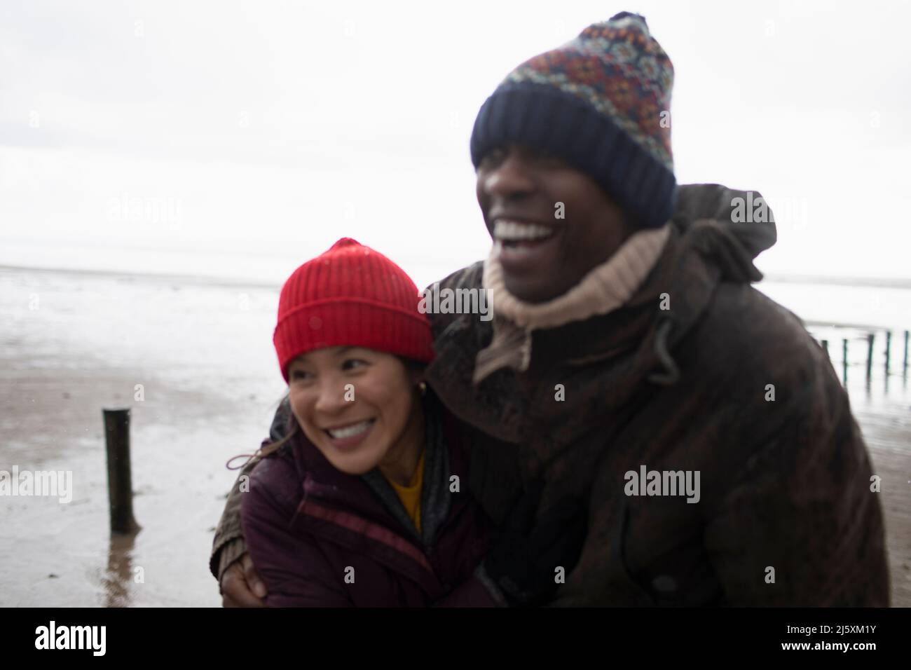 Un couple affectueux et joyeux, vêt de vêtements chauds qui s'embrasent sur la plage d'hiver Banque D'Images